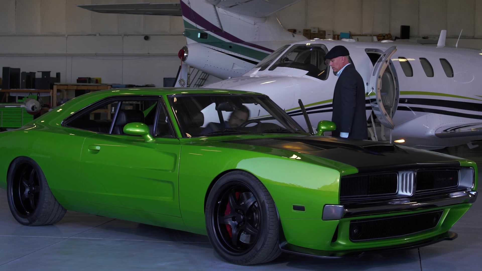 Green custom muscle car parked beside a private jet